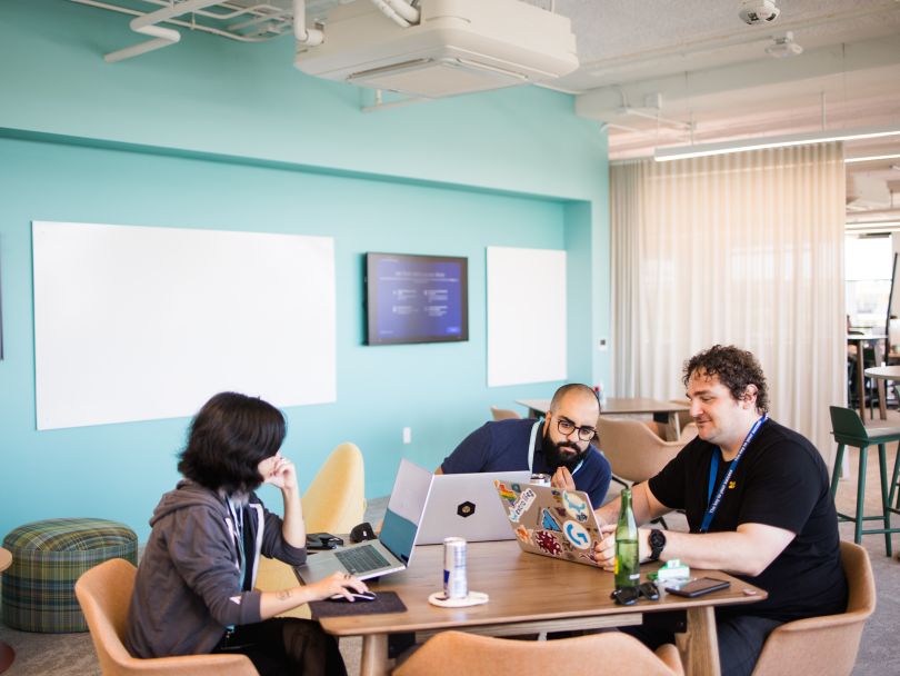 Three Atlassian team members work together at a table in the company's office